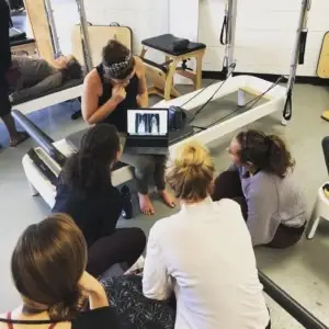 several women sitting down in a Pilates studio looking at an xray of a back on an iPad