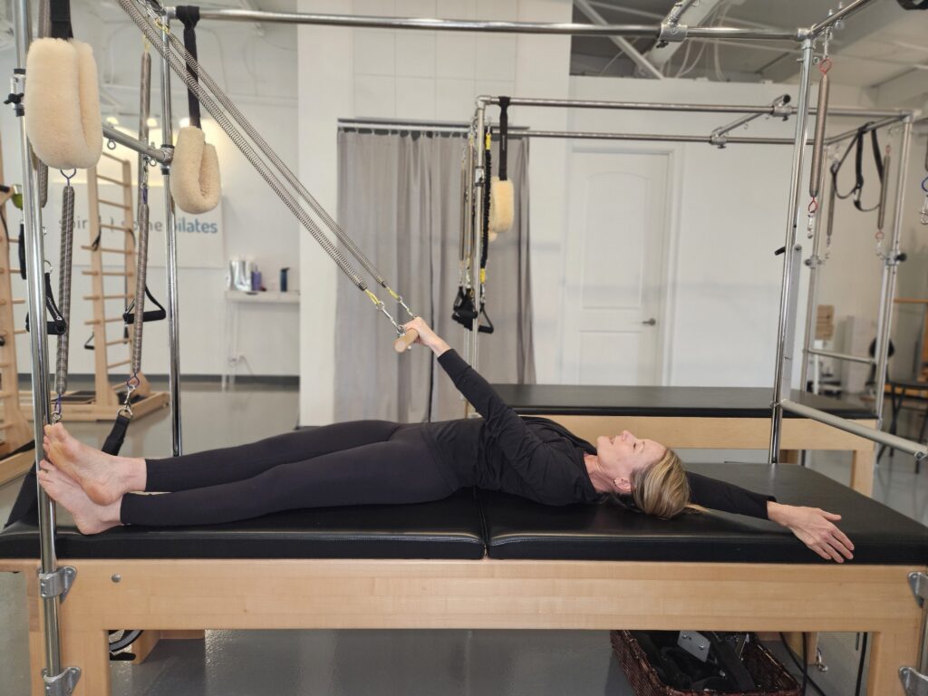 Pilates Instructor doing flexion exercise called Roll Down on Cadillac