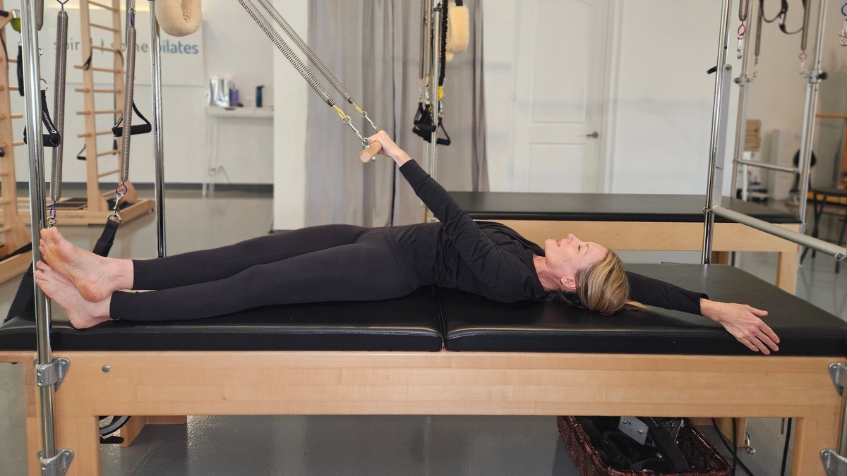 Pilates Instructor doing flexion exercise called Roll Down on Cadillac